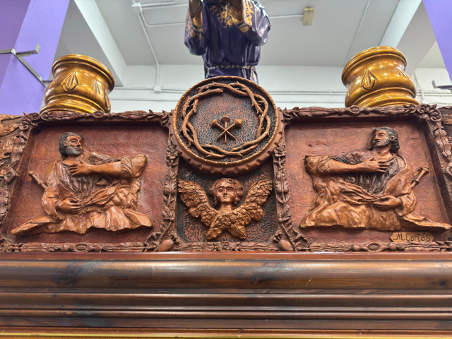 La parte frontal la preside el escudo de la cofradía que consta de los 3 clavos y la corona de espinas, justo debajo un ángel y sus lados dos apóstoles con cetros.